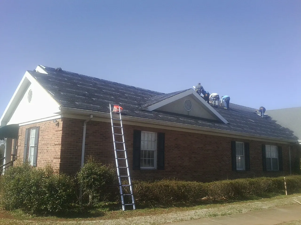 Crew tearing shingles off a brick ranch roof with a ladder set — Metal Roof Repair work by our crew in Franklin Furnace