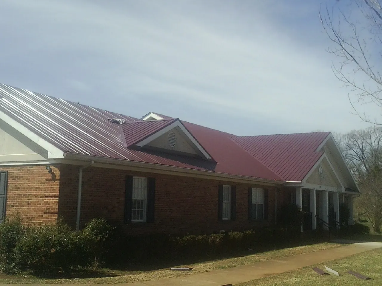 Red metal roof with gabled entries on a long brick building, from a Hail Damage Roof Repair job in Franklin Furnace