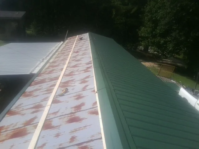 Old rusted panels beside newly installed green metal roofing — Wind Damage Roof Repair by Roofing Brothers in Franklin Furnace