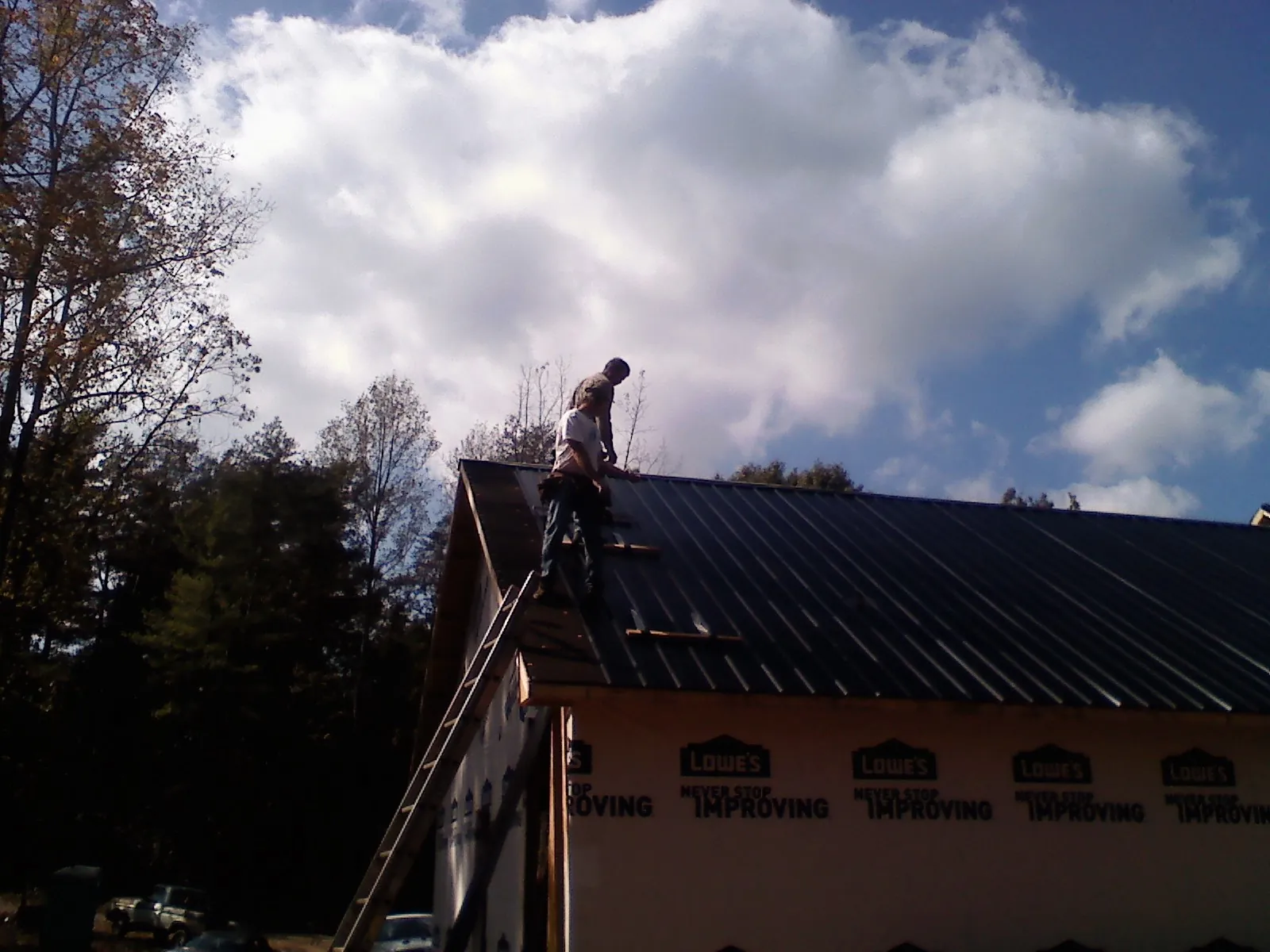 Roofer fastening dark metal panels high against a cloudy sky, from a Roof Inspection job in Franklin Furnace