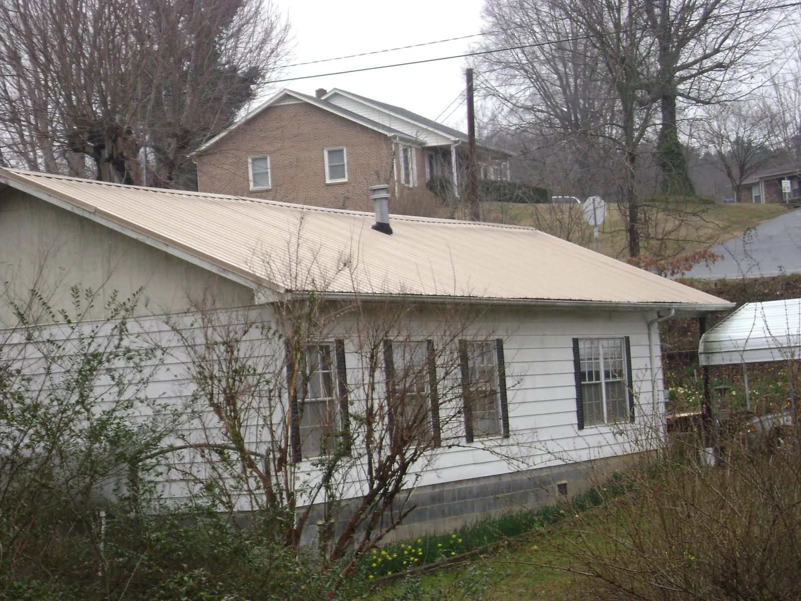 Tan metal roof on a white sided house set into a hillside — Commercial Roofing by Roofing Brothers in Franklin Furnace